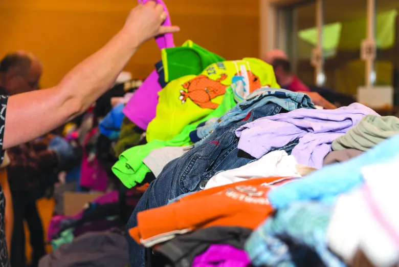 A pair of arms holds up a piece of clothing from a colorful pile of garments.
