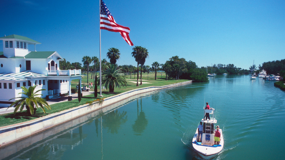 A boat sailing past a United States flag on a canal in Boca Grande, Florida.