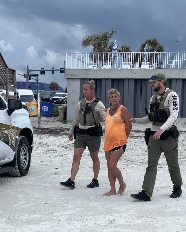 Deanna Harrell, accused of a driving a pickup truck into a tollbooth and killing the attendant, is led away in handcuffs from the Dunlawton beach ramp in Daytona Beach Shores.