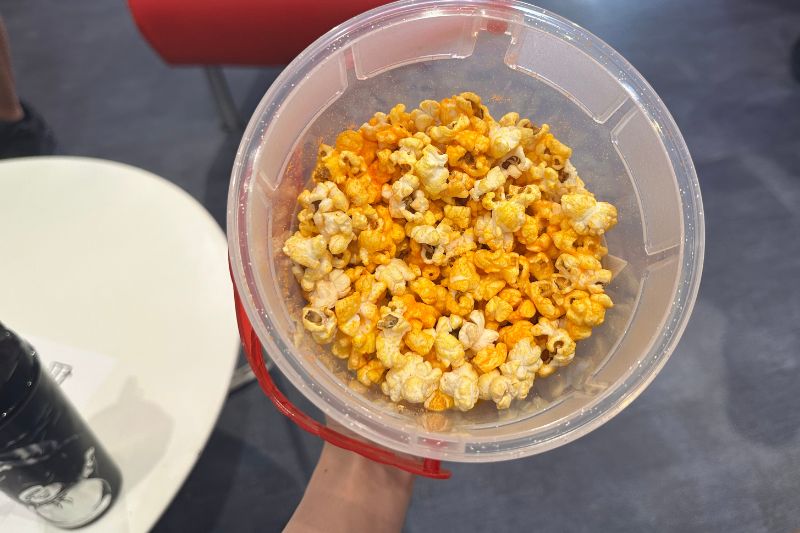 holding a popcorn bucket with orange colored seasoned popcorn