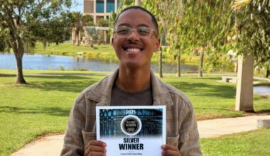 Josh Williams standing outdoors on a college campus holding a “Silver Winner” 2025 Collegiate Advertising Award certificate for Eastern Florida State College. A lake, palm trees, and campus buildings are visible in the background.