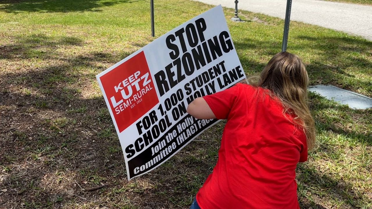 Demelza Hays puts up a sign in opposition to a a plan to build a private school in Lutz. (Spectrum News)