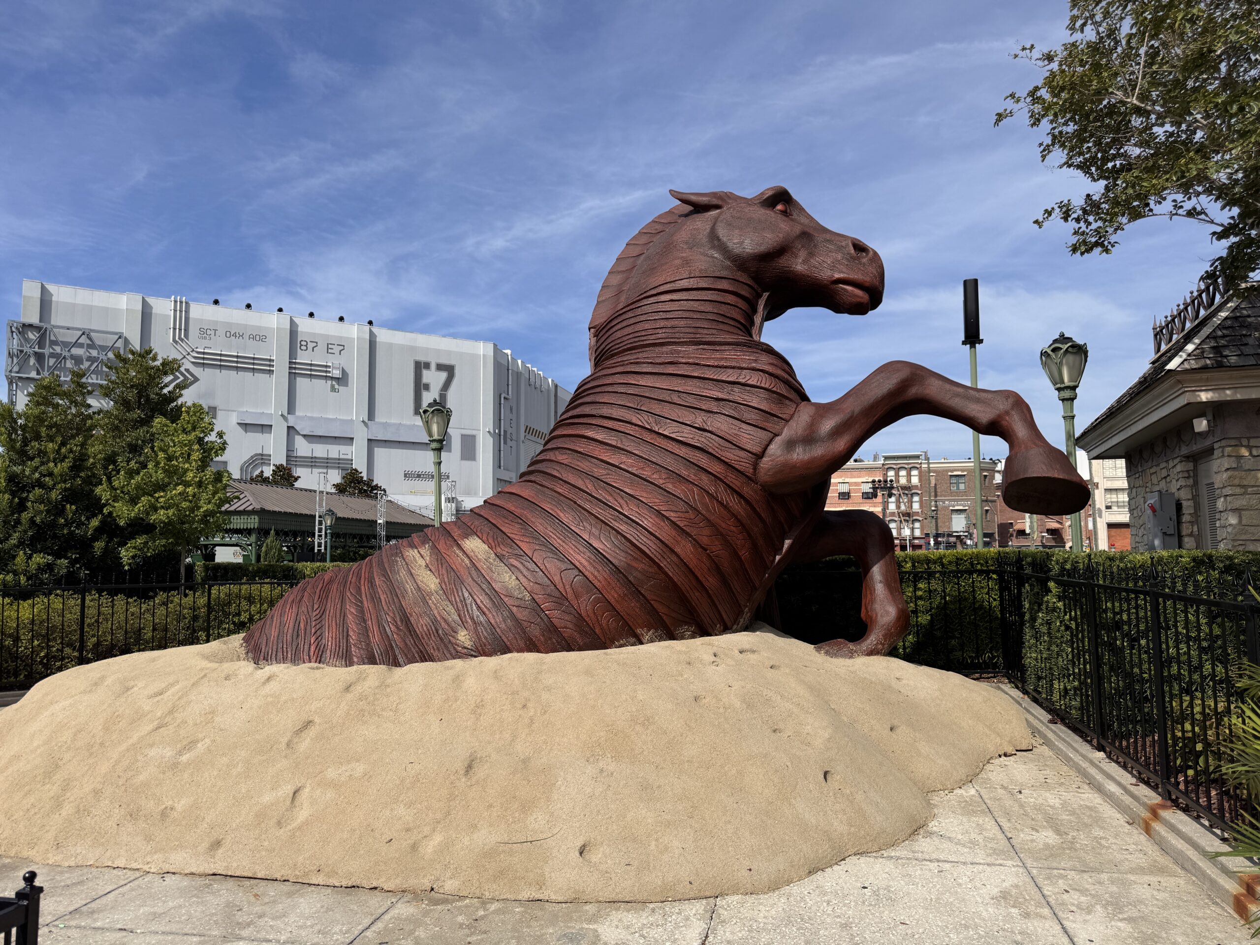 A large wooden horse sculpture, a reference to the Trojan Horse, emerges from the sand. This promotion is for The Odyssey, which follows the story of Odysseus, the king of Ithaca, on his journey to get home to his family after the Trojan War. It takes place in Ancient Greece.