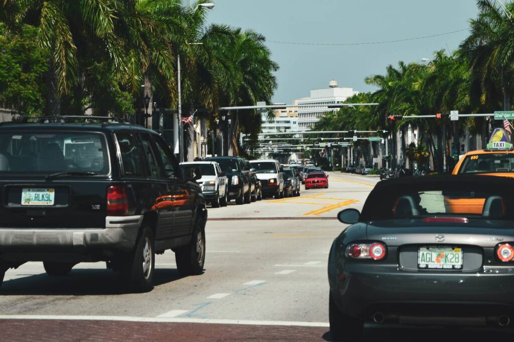 Street view of a bustling Miami road lined with palm trees and various cars during the day.