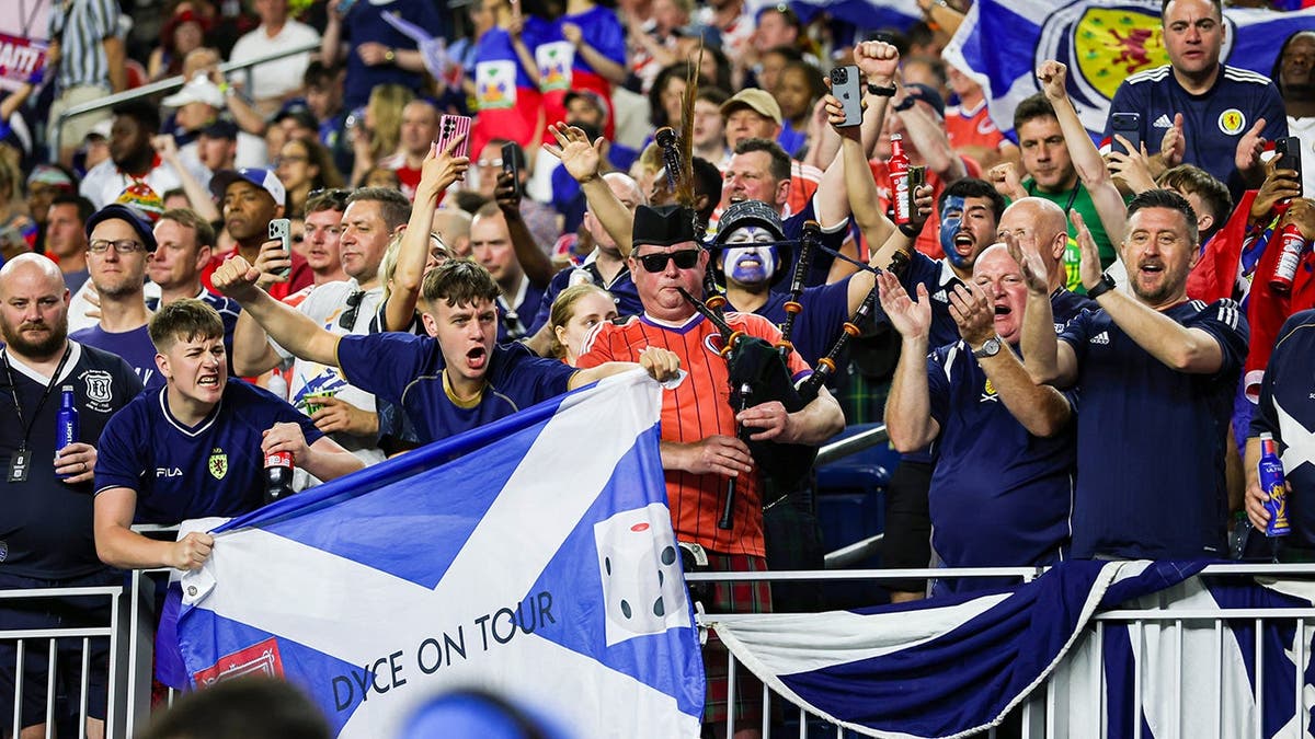 A group of Scottish soccer fans cheer on their team at a game in a stadium.