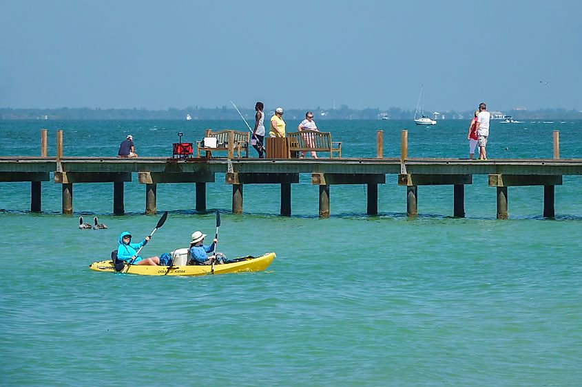 Two kayakers paddle near a public pier on Anna Maria Island, Florida