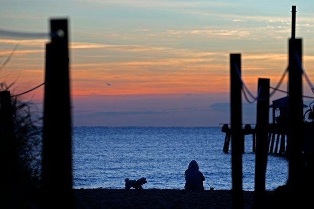 A woman sits with her dog at sunrise on Lauderdale-by-the-Sea beach early in the morning on Thursday. (Amy Beth Bennett / South Florida Sun Sentinel)