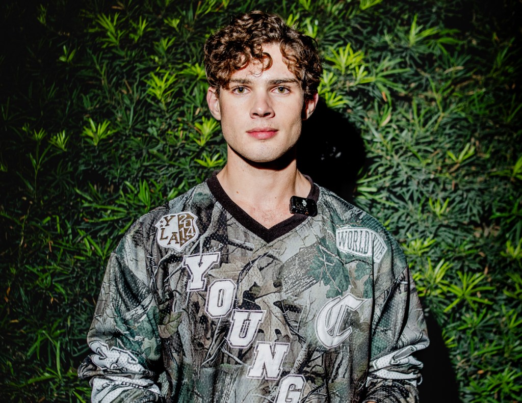 A photo of a young man posing in front of a bush