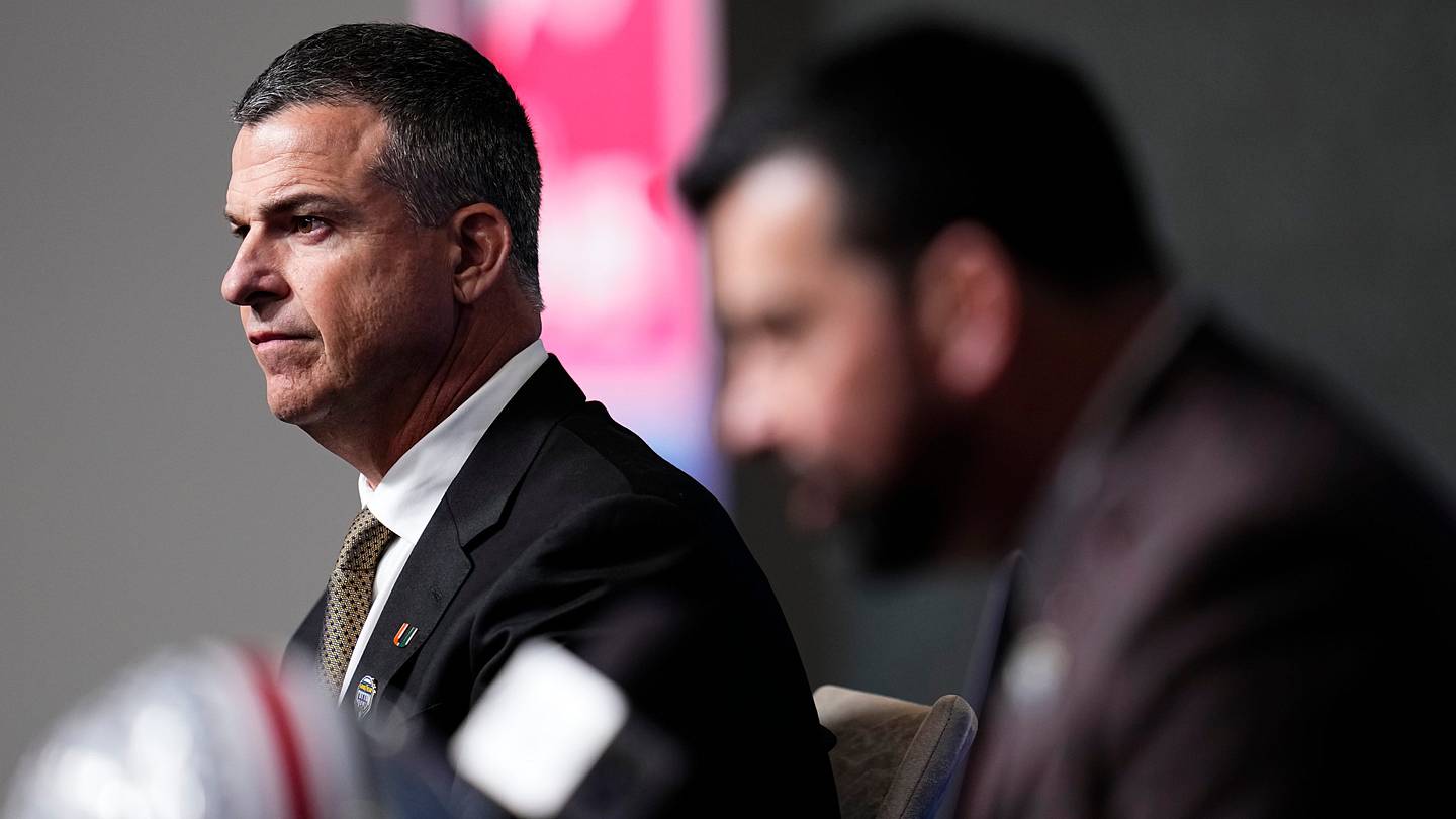 Miami (FL) Hurricanes head coach Mario Cristobal listens to Ohio State Buckeyes head coach Ryan Day talk to media during a Cotton Bowl press conference at AT&T Stadium in Arlington, Texas prior to their College Football Playoff quarterfinal matchup on Dec. 30, 2025.