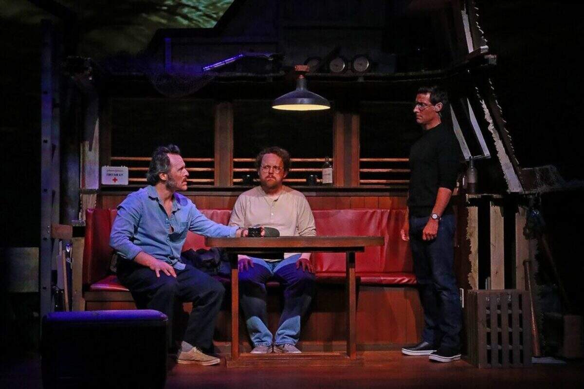 Iain Batchelor as Robert Shaw has a drink while Wesley Slade as Richard Dreyfuss and Adam Poole as Roy Scheider listen aboard the Orca in Actors’ Playhouse’s production of “The Shark Is Broken.”