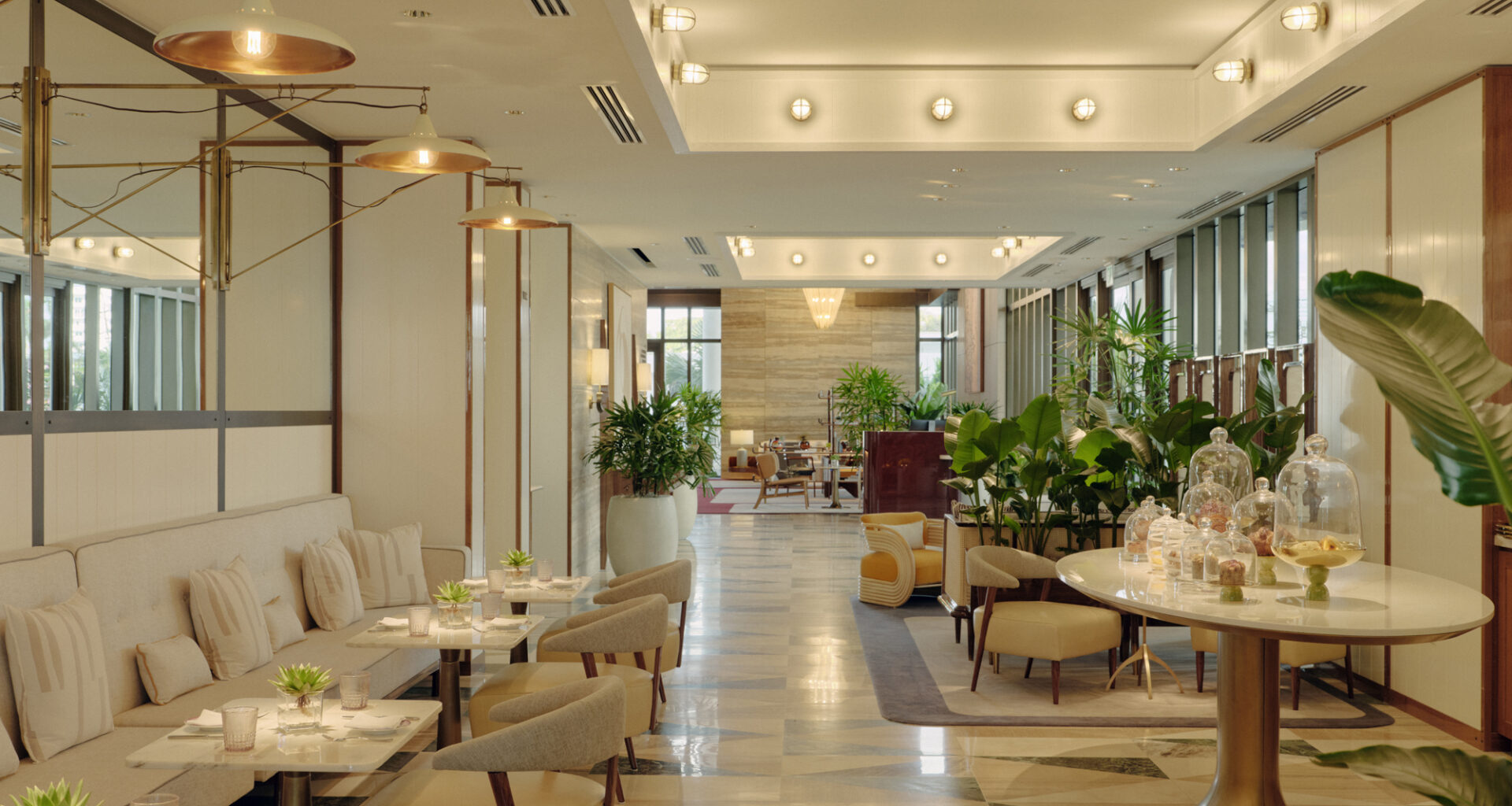 Honey Fitz café and champagne bar interior with beige seating, copper pendant lights, and tropical plants