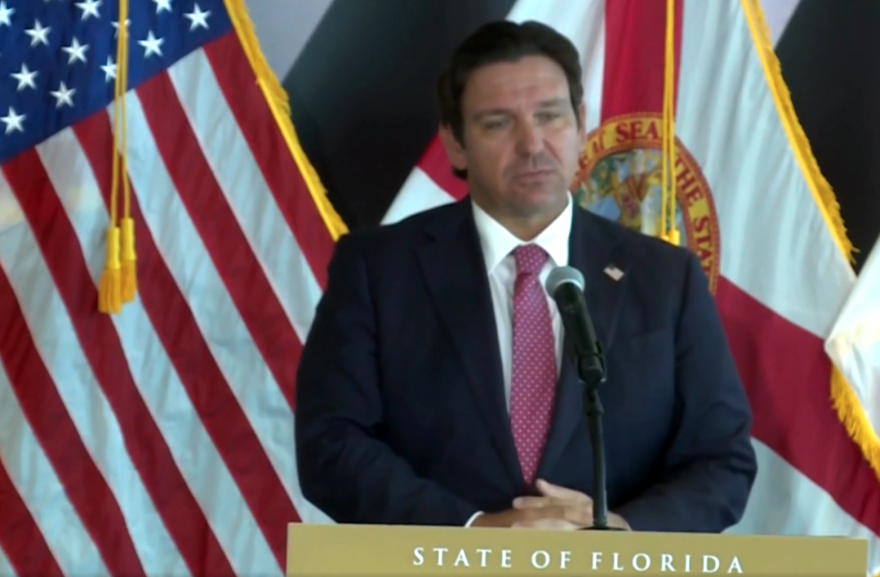 Gov. Ron DeSantis speaking at a podium in front of the American flag