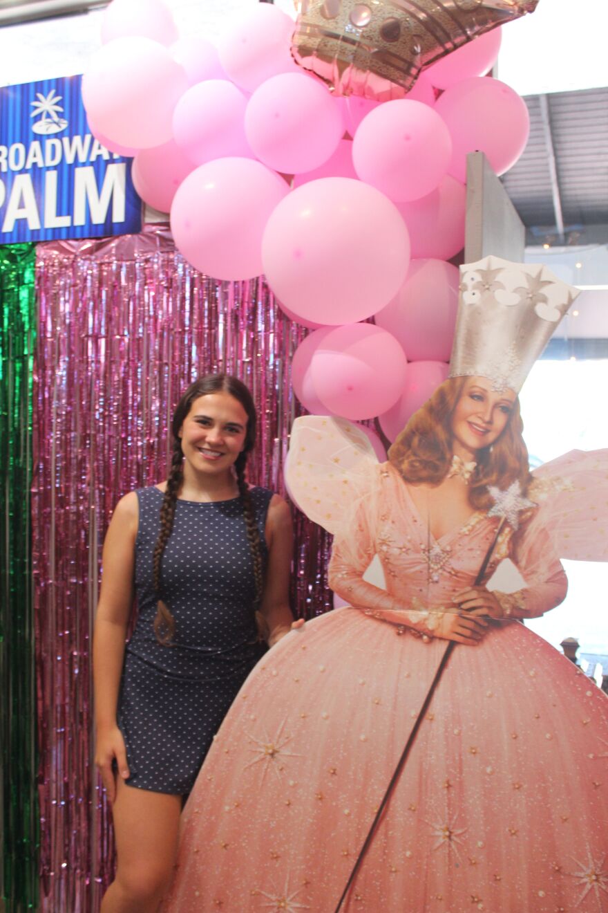 Rilyn Dick pictured with poster of Glinda in lobby of Broadway Palm Dinner Theatre.
