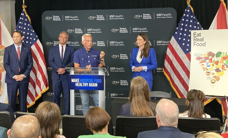 Man speaks at podium surrounded by three other people