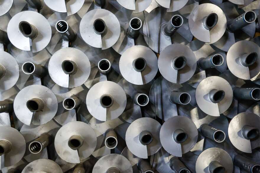A close up of silver helical pilings, which look like long silver beams with a pointed end and spiraling metal components.