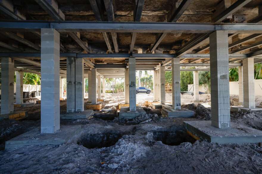 The underside of a home being lifted, with exposed beams and holes in the ground.