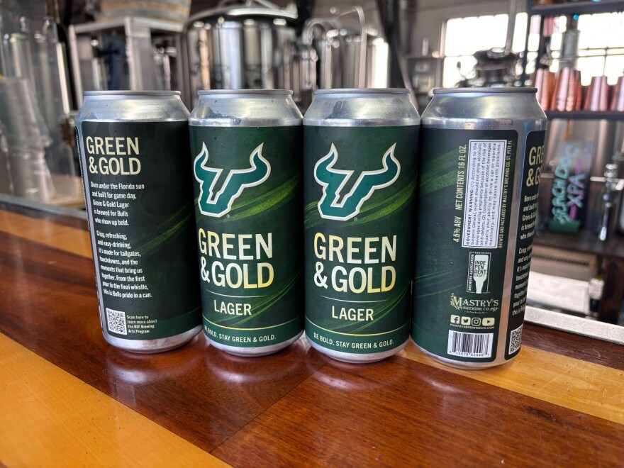 Four tall boy-sized beer cans with a green and gold palette and the “green and gold lager” name. the wrap is simple and uses the u-shaped bull horns logo.