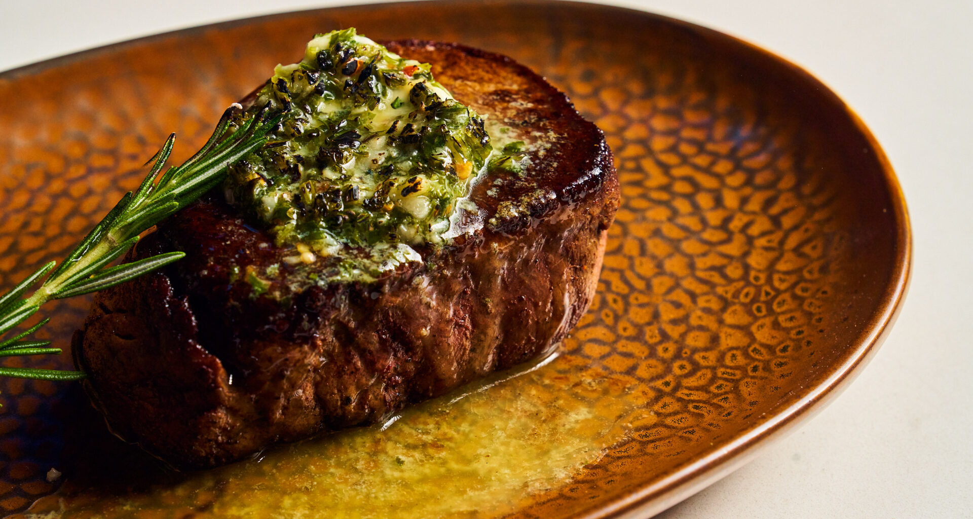 a filet mignon with green sauce on a gold plate