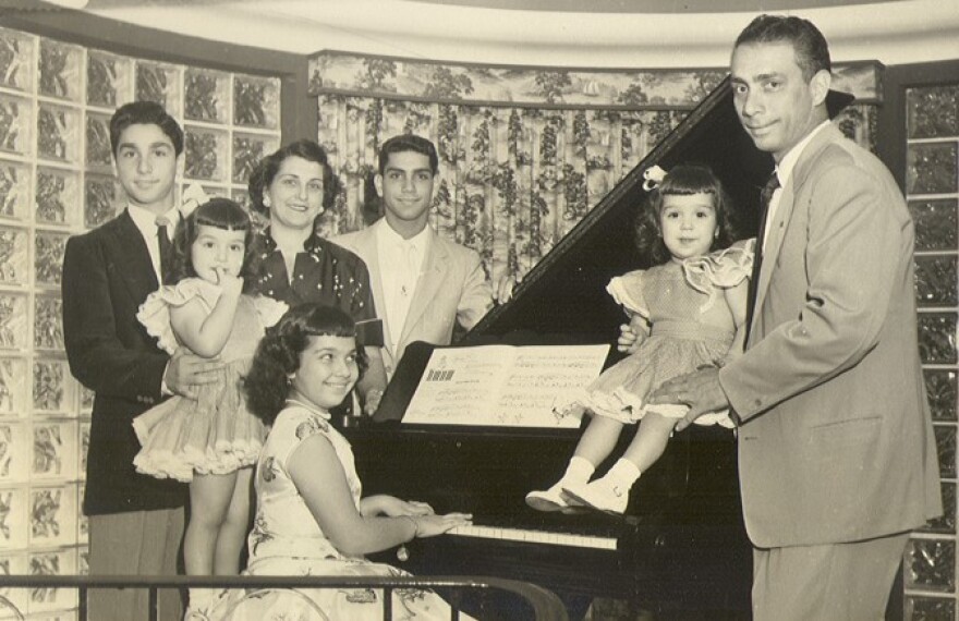 Black and white photo of family in a living room next to the piano