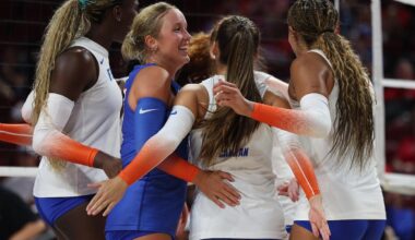 Two female volleyball athletes, one in white and one in orange Florida uniforms, hugging