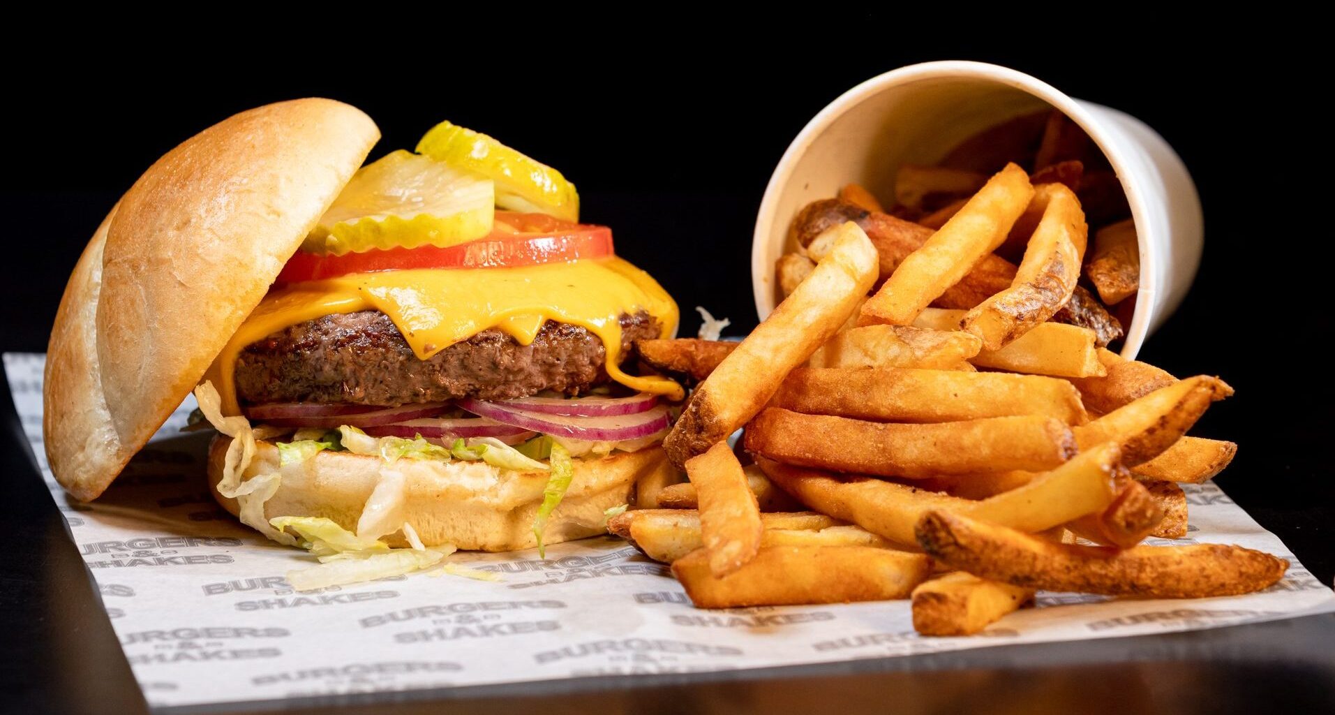 a cheeseburger with toppings and a side of fries with a black background