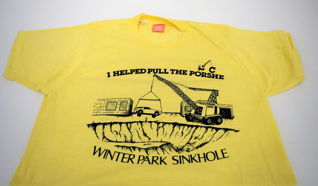 Yellow t-shirt with illustration and text reading "I helped pull the porsche WINTER PARK SINKHOLE