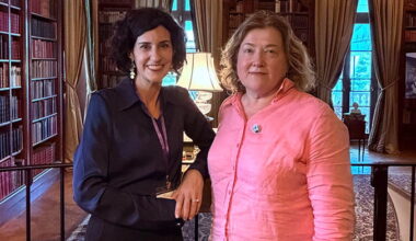 Two adult women smiling and posing together in a large, tidy private library in the historic Edith Wharton estate.