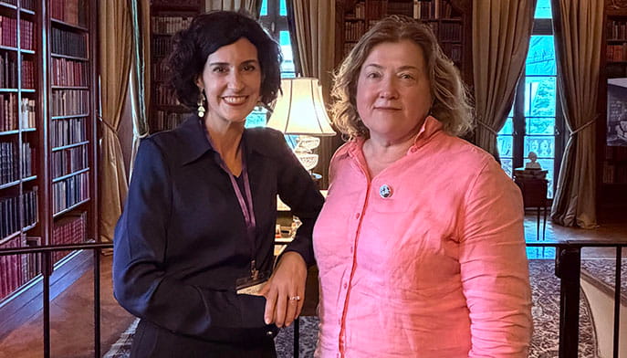 Two adult women smiling and posing together in a large, tidy private library in the historic Edith Wharton estate.