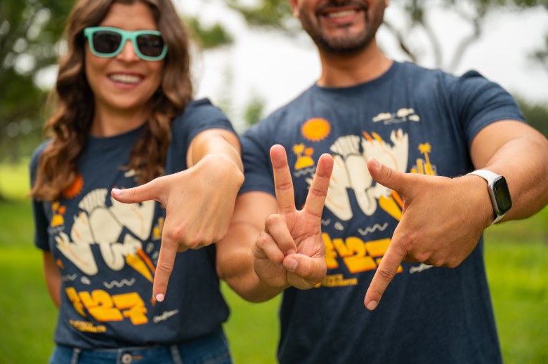 Two people wearing 727 shirts make hand signs forming a 7 2 and 7