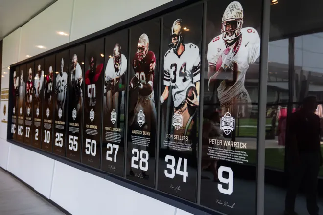 A wall with photographs and small biographies of players a part of the Hall of Fame is displayed in a long hallway inside the Florida State University Dunlap Football Center.