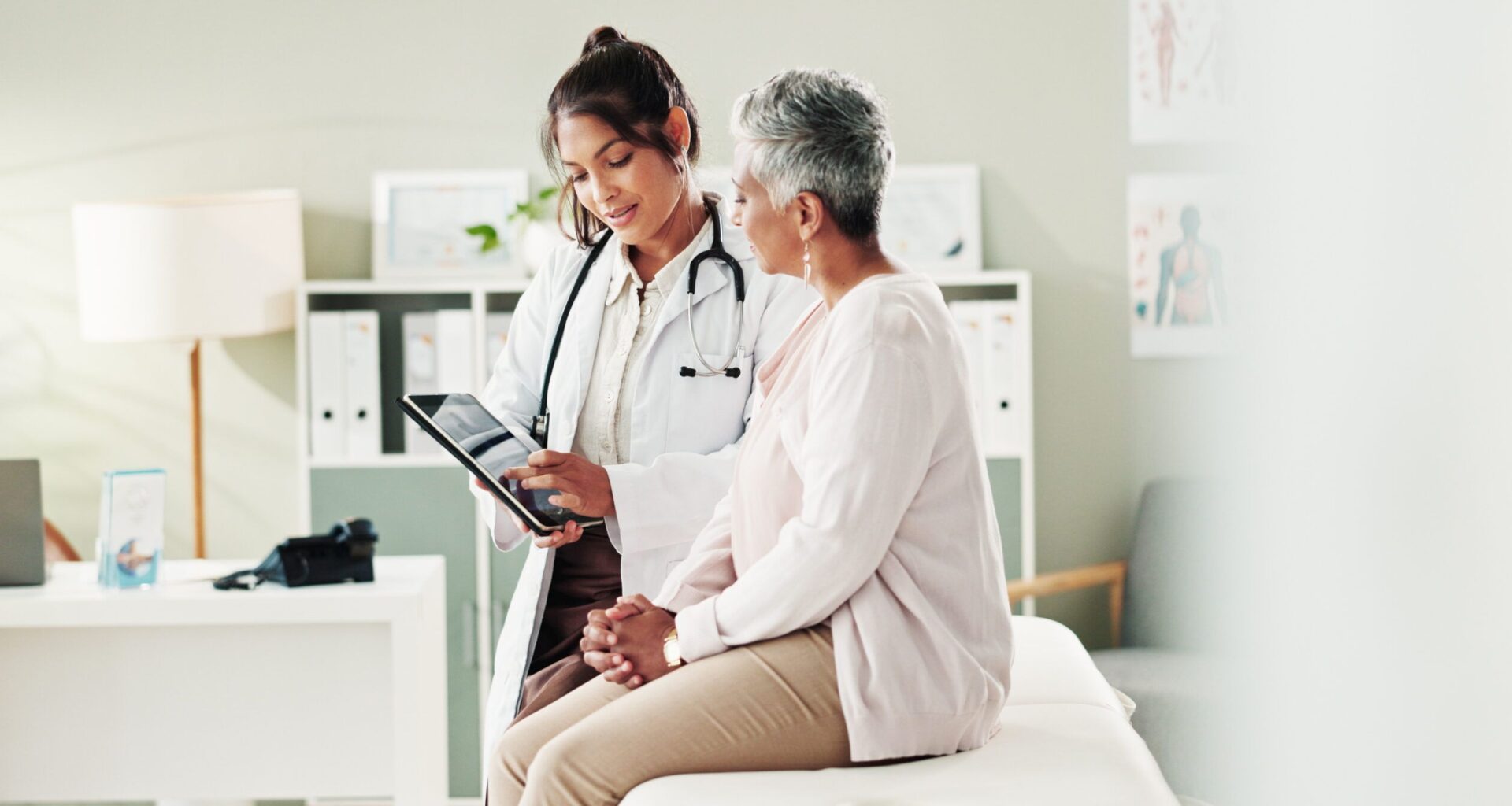 Doctor reviews medical information on a tablet with a patient during an outpatient clinic visit.