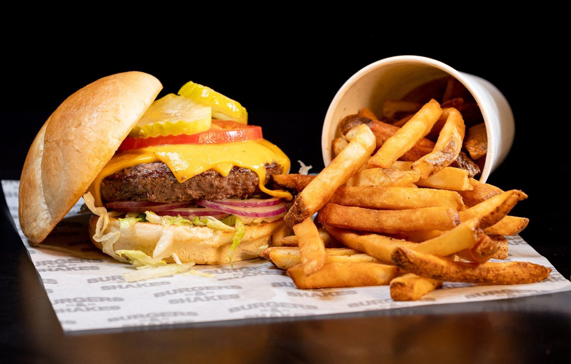 a cheeseburger with toppings and a side of fries with a black background