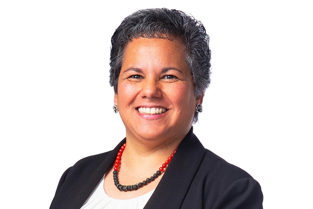 Portrait of smiling woman with gray short hair wearing black business jacket, black and red beaded necklace and white under shirt on a white backdrop