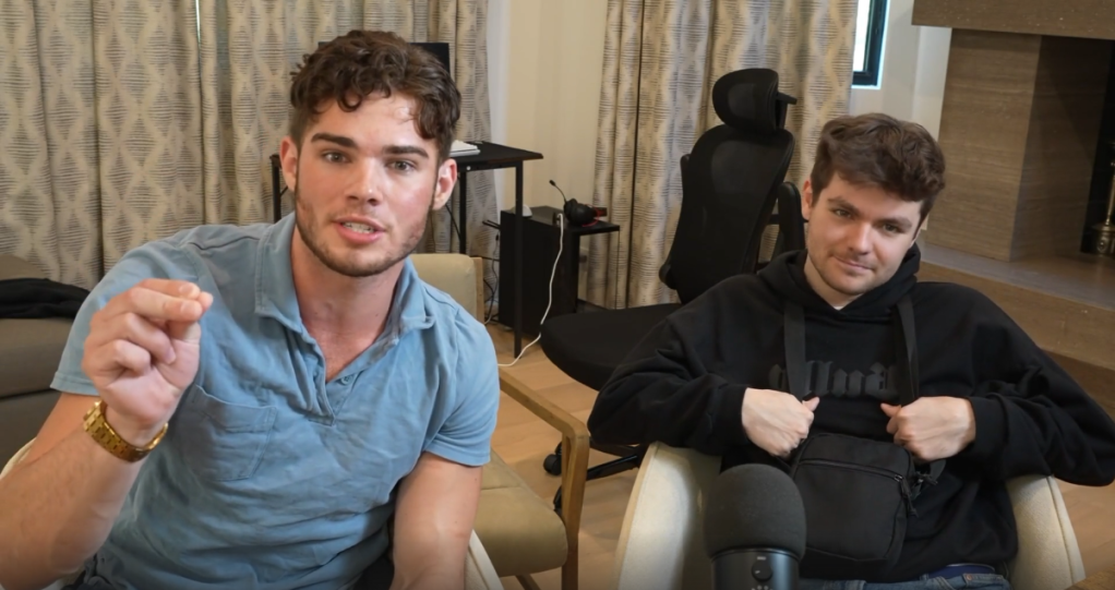 A photo of two men sitting in chairs inside of a room speaking to a camera.
