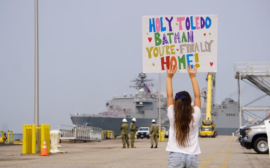 A girl holds up a sign and looks at a ship in the distance.