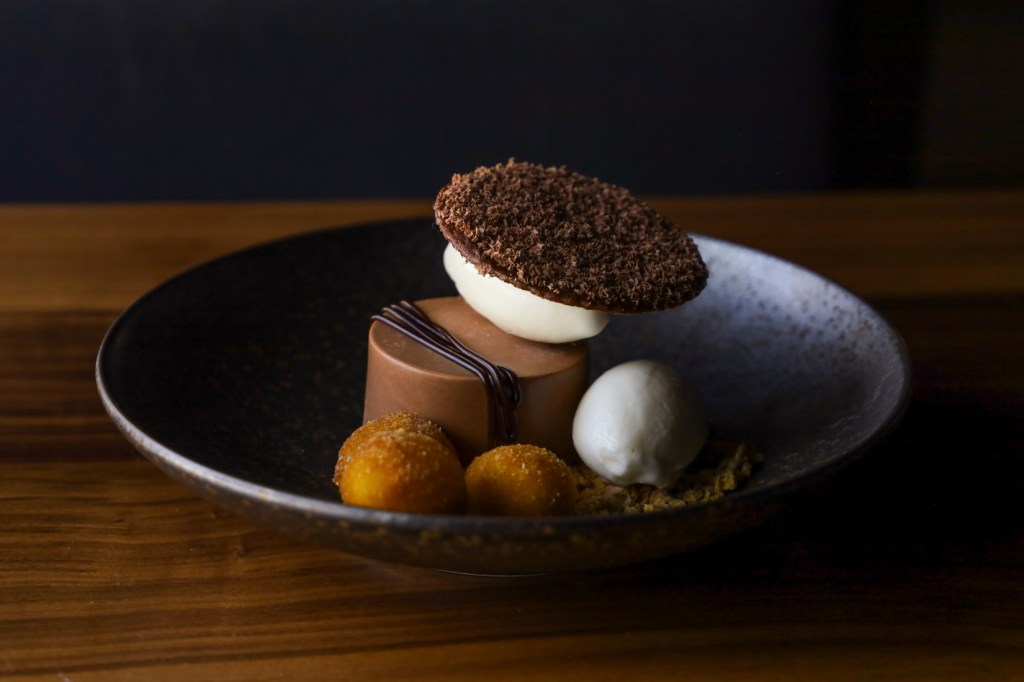 a brown mousse with toppings in a black bowl on a brown table