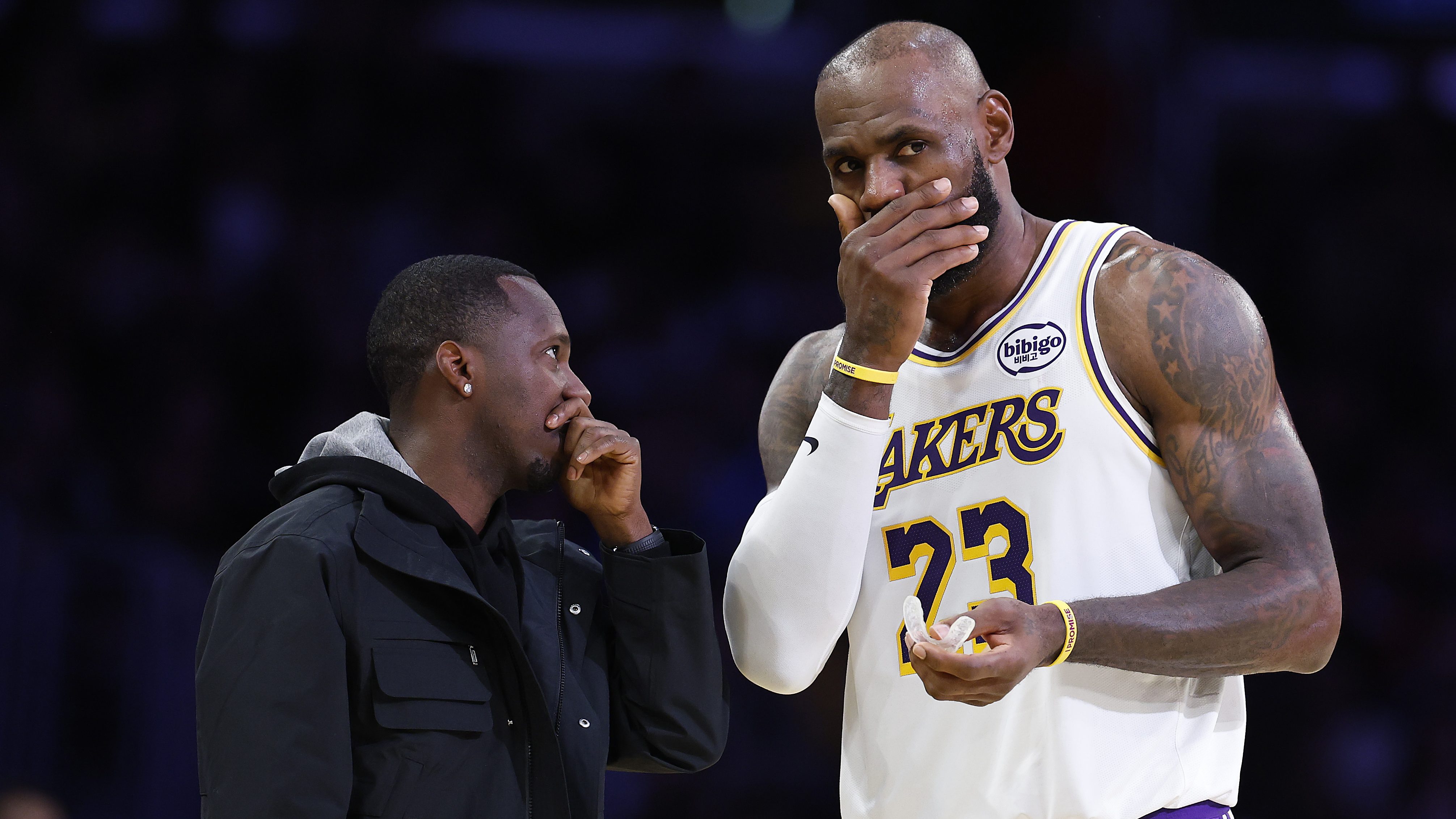 LeBron James covers his mouth while speaking with agent Rich Paul during a Lakers game.