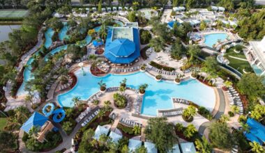 Hilton Orlando - Pool Aerial view of a large resort pool area with multiple swimming pools, water slides, lounge chairs, cabanas, and surrounding greenery.