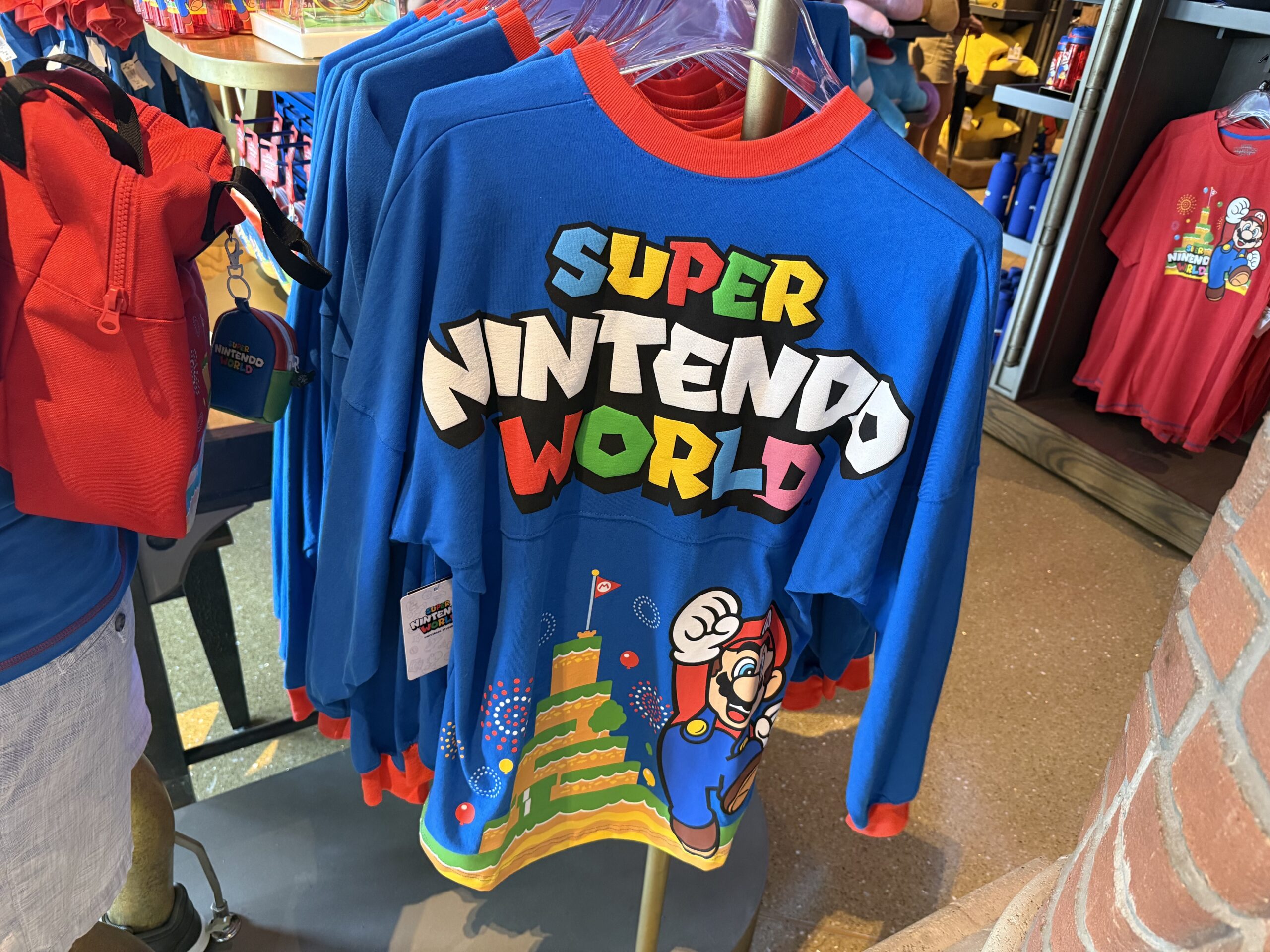This spirit jersey is blue with a red collar and sleeve cuffs and. The front has the Super Nintendo World logo, while the back has Mario and Mount Beanpole.