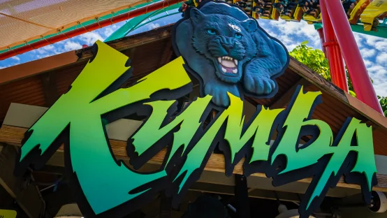 Close-up of the official green and yellow Kumba roller coaster sign featuring a blue roaring panther emblem on a wooden entrance roof.