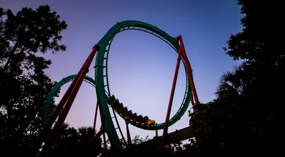 The silhouette of Kumba's iconic vertical loop with a yellow coaster train at the bottom, captured against a purple and blue twilight sunset sky.