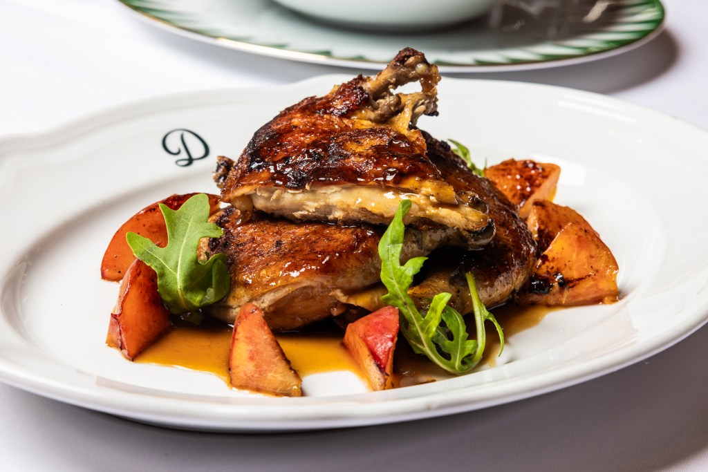 a chicken dish on a white plate with sauce and garnishes on a white table