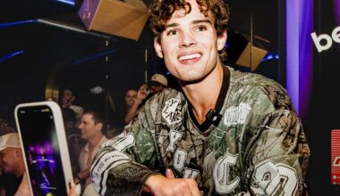 A photo of a young man smiling while crouching on a stage in a nightclub.