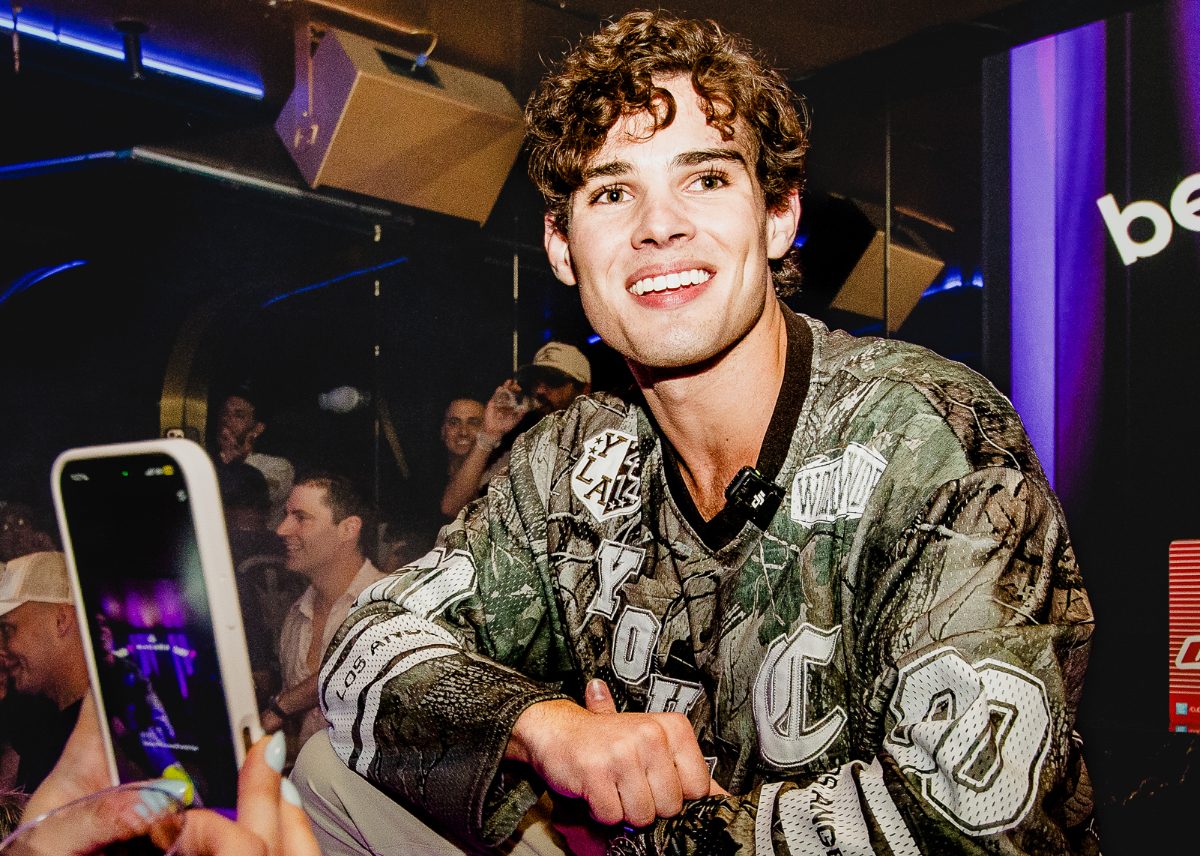 A photo of a young man smiling while crouching on a stage in a nightclub.