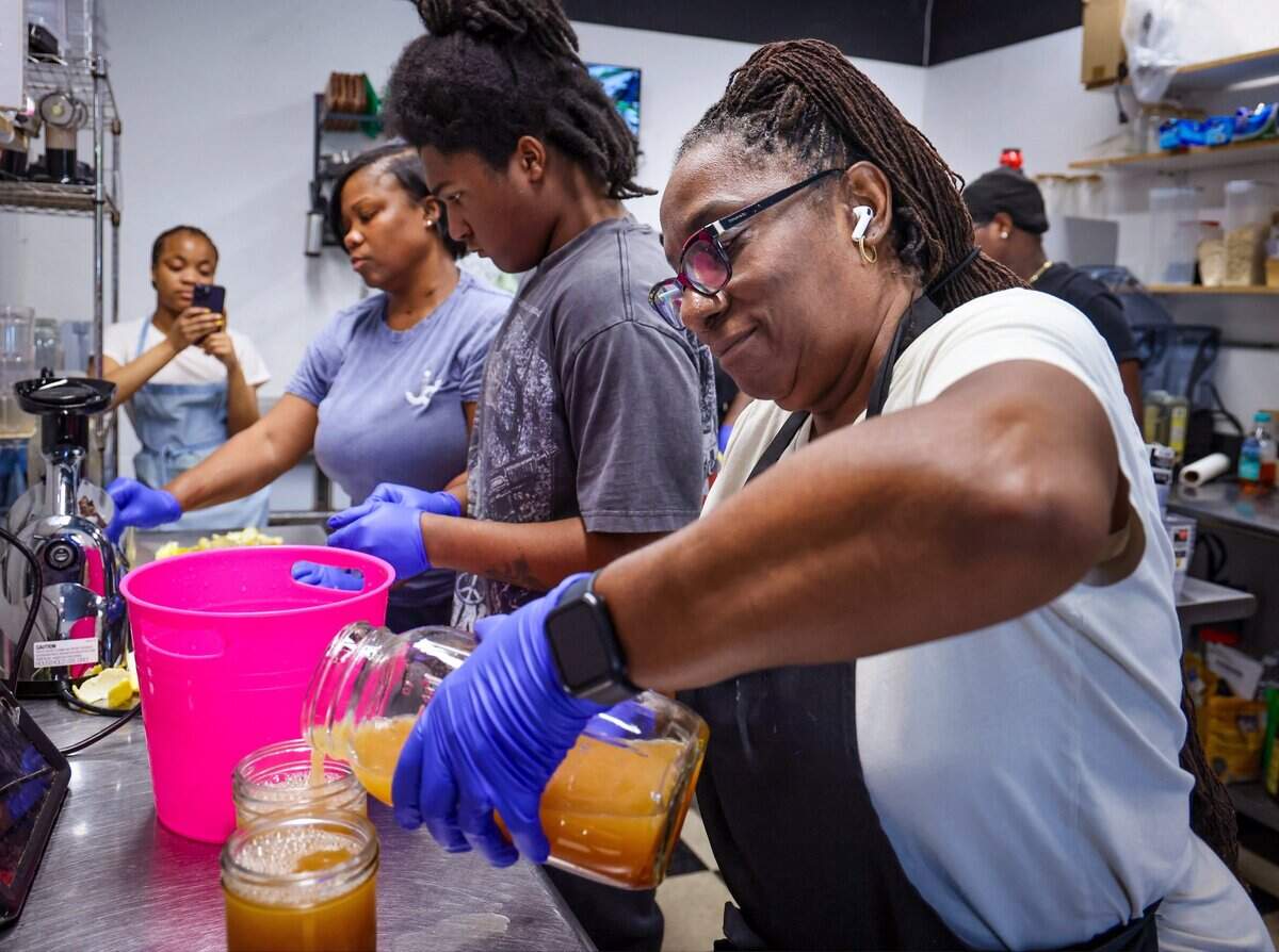 Intern Teresa Washington, left, records a video as JuiceDefined owner Fathiyyah “Tia” Doster, intern Darin Green, and Mae Mike, right, prepare a large order, Thursday, July 30, 2026, in downtown Opa-locka, Fla.
