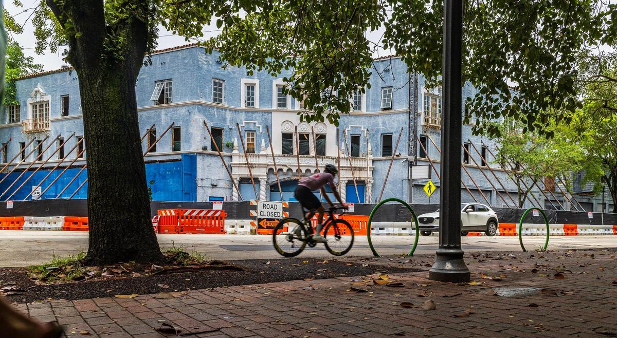A cyclist rides on Main Highway past the historic Coconut Grove Playhouse in 2024. The theater’s facade was reinforced with temporary beams after a contractor’s error during interior demolition work caused a partial ceiling collapse.