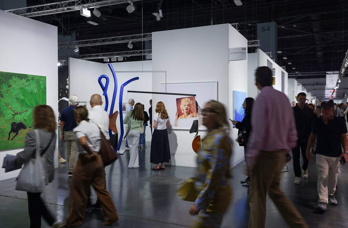 Fair goers stop and navigate pass The Modern Institute booth engaging with Anne Collier “Album (Marilyn Monroe), 2015 and  Martin Boyce's piece “Yesterday's Tomorrows”, 2025 painted steel, chain, and wire at Wednesday's VIP opening at Art Basel Miami Beach on its opening day of the 23rd annual Art Basel in Miami Beach, Florida on Wednesday, December 3, 2025. The 23rd edition of Art Basel Miami Beach kicked off Wednesday as VIPs surveyed the collection of international and local galleries.