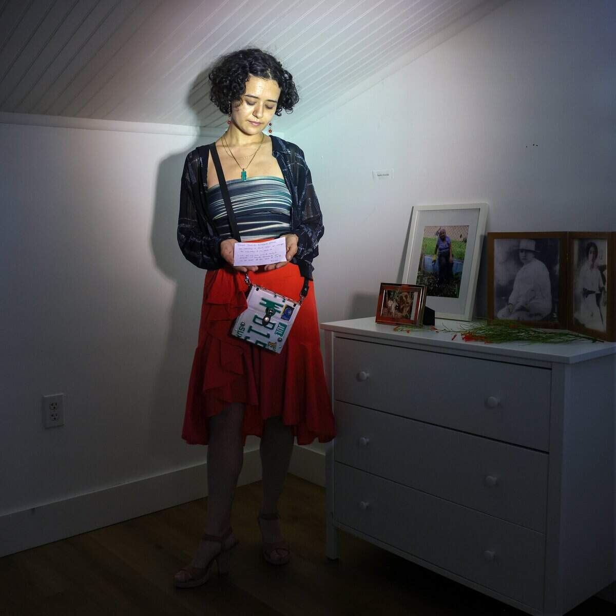 Artist and community organizer Claribel Avila, stands in the attic as she holds her note she wrote while attending the “Turn of A Century art event hosted by friends - Sophia Corugedo, and Sofia Villalonga, at the 100-year-old home, which is slated for demolition after being sold to a developer on Monday, July 13, 2026, in Miami, Fla. Pictured is a photograph of the original owner of the home - Leonard H. Dasher. Franco explored the past history of the home in her installation. The gathering features artists, performers and dancers saying farewell to the house before the owners move out by July 15.
