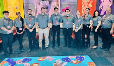 Chuck E. Cheese team, mostly young adults, stand in a party room with character posters and vibrant carpet at the family fun center.