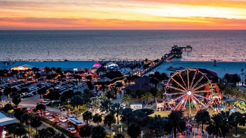 a waterfront beach festival at sunset. a large Ferris wheel is visible in the foreground.